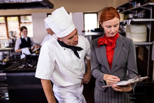 Female manager and male chef writing on clipboard in kitchen